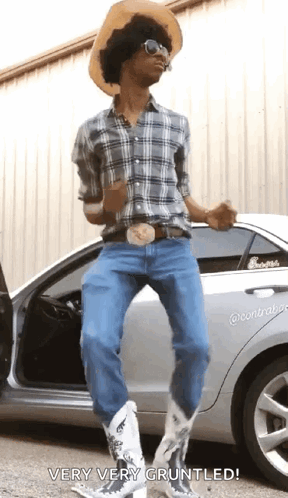 A Man In A Cowboy Hat And Cowboy Boots Is Standing Next To A Car . GIF