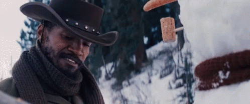 A Man In A Cowboy Hat And Scarf Is Standing In The Snow Looking At Something GIF