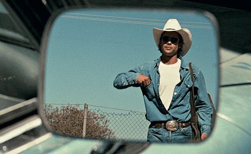 A Man In A Cowboy Hat And Sunglasses Is Reflected In A Car Mirror GIF