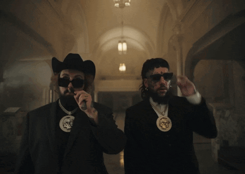 A Man In A Cowboy Hat And Sunglasses Stands Next To Another Man GIF