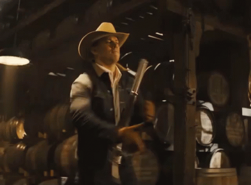 A Man In A Cowboy Hat Holds A Gun GIF