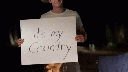 A Man In A Cowboy Hat Holds A Sign That Says It 'S My Country GIF