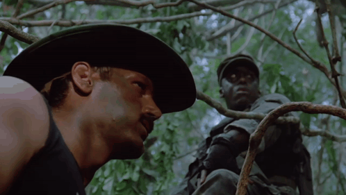 A Man In A Cowboy Hat Is Looking At Another Man GIF