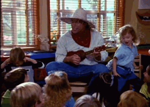 A Man In A Cowboy Hat Is Playing A Guitar In Front Of Children GIF