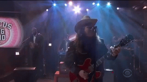 A Man In A Cowboy Hat Is Playing A Red Guitar GIF