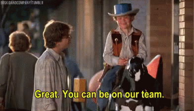 A Man In A Cowboy Hat Is Riding A Horse While Another Man Stands Behind Him . GIF