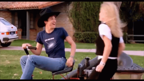 A Man In A Cowboy Hat Is Riding A Lawn Mower GIF