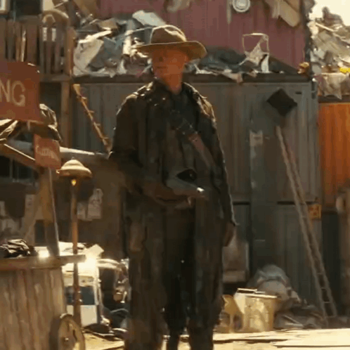 A Man In A Cowboy Hat Is Standing In Front Of A Sign That Says Clothing GIF