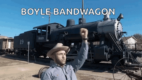 A Man In A Cowboy Hat Is Standing In Front Of A Train That Says Boyle Bandwagon On It GIF