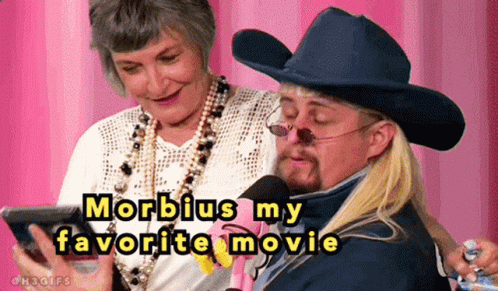 A Man In A Cowboy Hat Is Talking Into A Microphone While A Woman Watches GIF