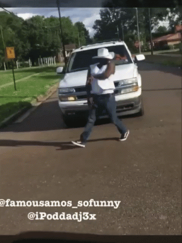 A Man In A Cowboy Hat Is Walking Across A Street In Front Of A White Suv GIF