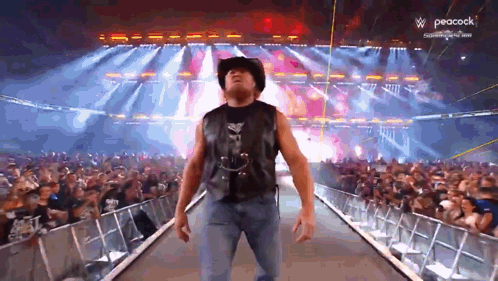 A Man In A Cowboy Hat Is Walking Down A Ramp In Front Of A Crowd With Peacock In The Background GIF