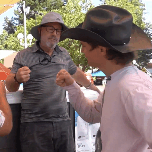 A Man In A Cowboy Hat Shakes Hands With A Man In A Pink Shirt GIF