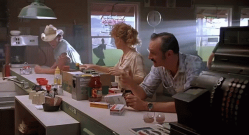 A Man In A Cowboy Hat Sits At A Counter In A Diner Talking To A Woman And Another Man GIF