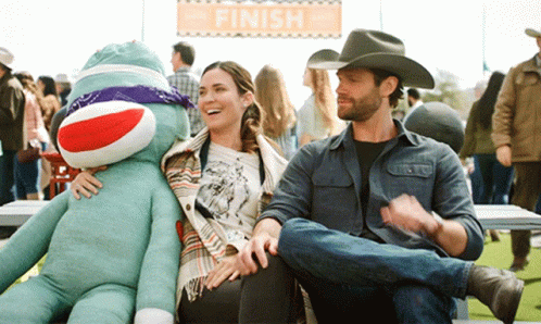 a man in a cowboy hat sits next to a woman holding a sock monkey under a finish sign