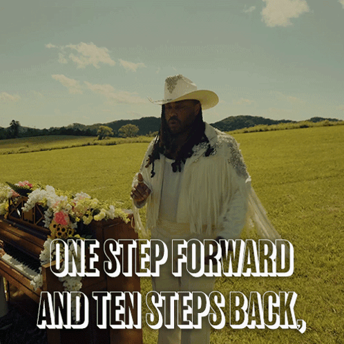 A Man In A Cowboy Hat Stands In A Field Next To A Piano With The Words One Step Forward And Ten Steps Back GIF
