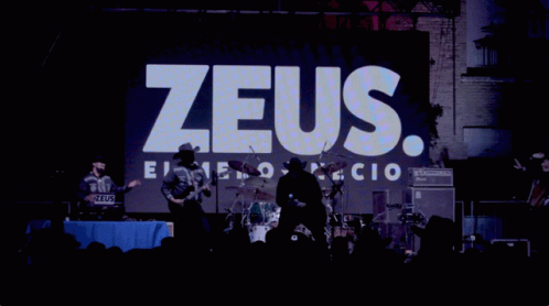 A Man In A Cowboy Hat Stands In Front Of A Zeus Sign GIF