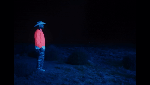 A Man In A Cowboy Hat Stands Next To A Glowing Horse In The Dark GIF