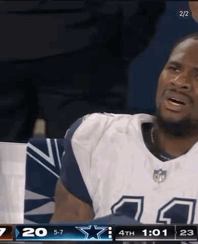 A Man In A Cowboys Jersey Is Sitting In The Stands During A Game . GIF