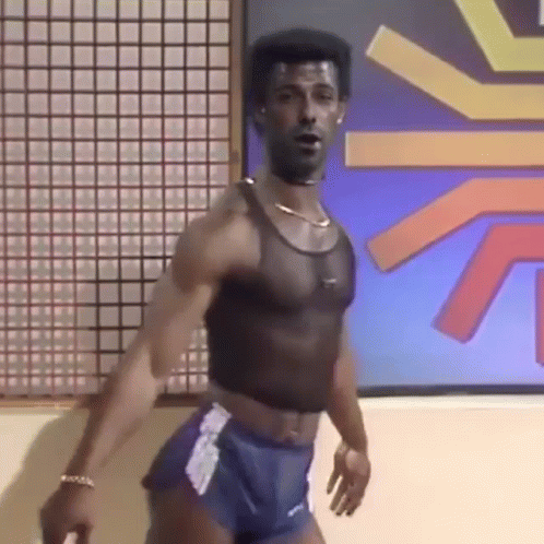A Man In A Crop Top And Shorts Is Standing In Front Of A Wall . GIF