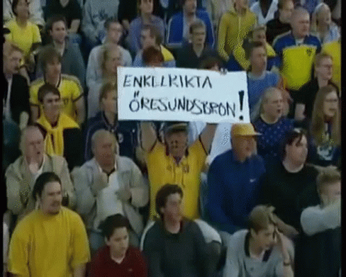 A Man In A Crowd Holds Up A Sign That Says " Enklrikta " On It GIF
