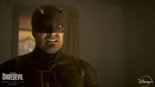 A Man In A Daredevil Costume Is Smiling In A Dark Room . GIF