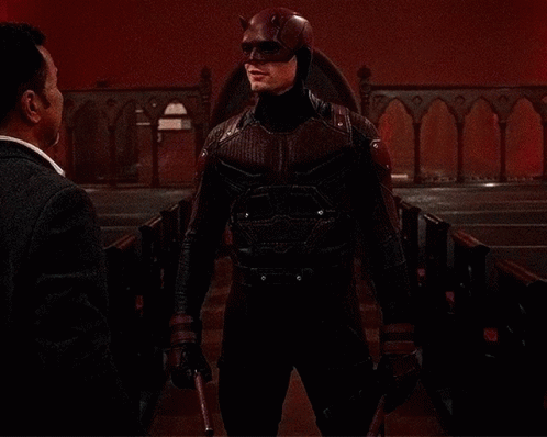A Man In A Daredevil Costume Is Talking To Another Man In A Church GIF
