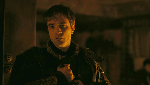 A Man In A Dark Room Holds A Sword In His Hand GIF