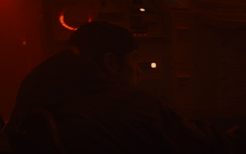 A Man In A Dark Room With A Red Background GIF