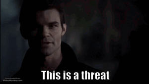 A Man In A Dark Room With The Words This Is A Threat Below Him GIF