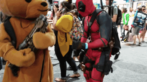 A Man In A Deadpool Costume Stands Next To A Teddy Bear GIF