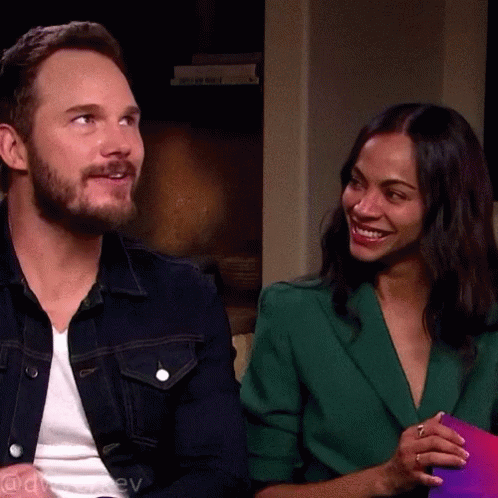 A Man In A Denim Jacket And A Woman In A Green Jacket Are Sitting Next To Each Other GIF
