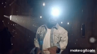 A Man In A Denim Jacket Is Dancing In Front Of A Projector Screen . GIF