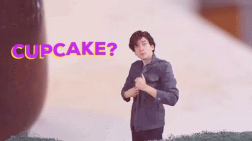 A Man In A Denim Jacket Is Holding A Cupcake In Front Of A Sign That Says Cupcake . GIF