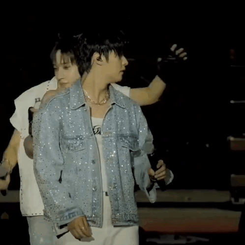 A Man In A Denim Jacket Is Holding A Microphone On A Stage GIF