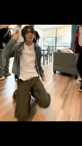 A Man In A Denim Jacket Is Kneeling Down And Dancing In A Room . GIF