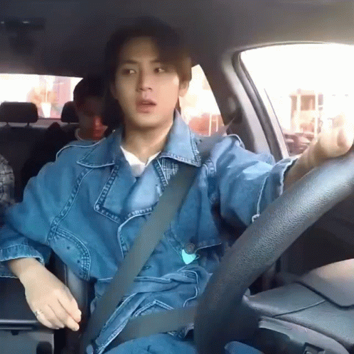 A Man In A Denim Jacket Is Sitting In A Car With A Seat Belt On . GIF