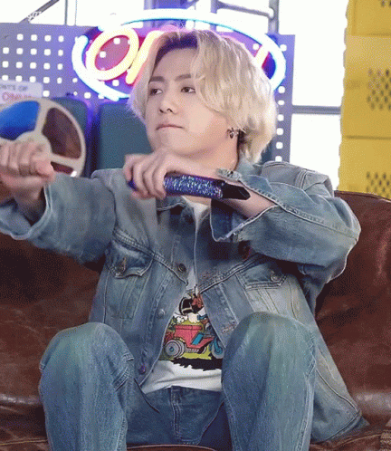 A Man In A Denim Jacket Is Sitting On A Couch Holding A Remote Control GIF