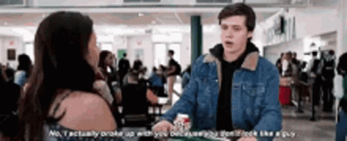 A Man In A Denim Jacket Is Talking To A Woman In A Crowded Room . GIF