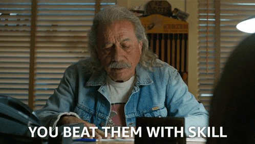 A Man In A Denim Jacket Sits At A Desk With The Words " You Beat Them With Skill " Above Him GIF