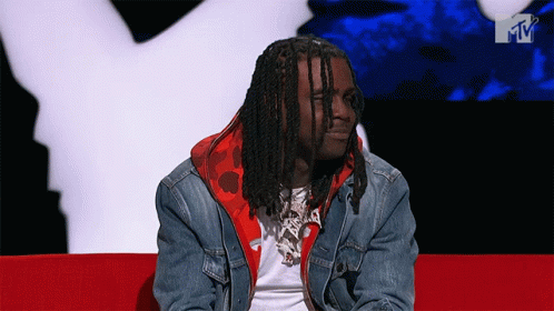 A Man In A Denim Jacket Sits On A Red Couch GIF