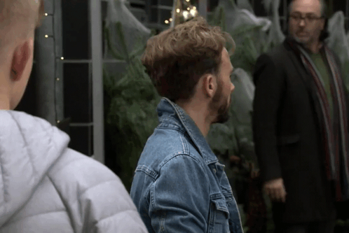 A Man In A Denim Jacket Stands Next To Another Man In A Suit GIF