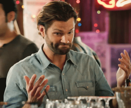 a man in a denim shirt is sitting at a bar with his hands up