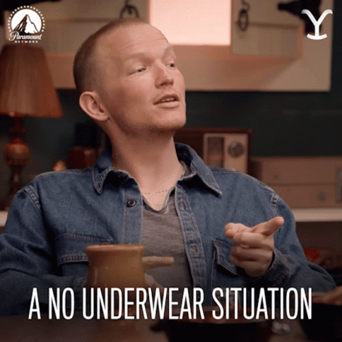A Man In A Denim Shirt Is Sitting At A Table With A No Underwear Situation Written Below Him GIF