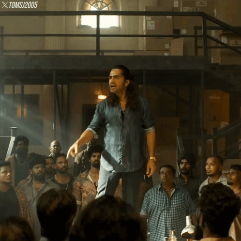A Man In A Denim Shirt Stands In Front Of A Crowd Of People With A Toms 2005 Watermark GIF