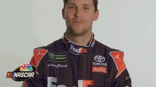 A Man In A Fedex Racing Suit Is Standing In Front Of A Nascar Logo . GIF
