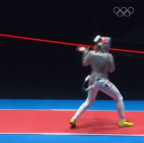 A Man In A Fencing Uniform Is Standing On A Red And Blue Court . GIF