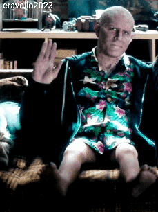 A Man In A Floral Shirt Is Sitting On A Couch And Waving His Hand GIF