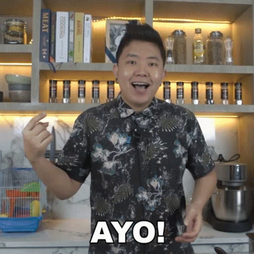 A Man In A Floral Shirt Says Ayo In Front Of A Bookshelf GIF