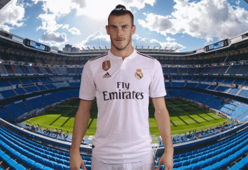 A Man In A Fly Emirates Jersey Stands In Front Of A Soccer Field GIF